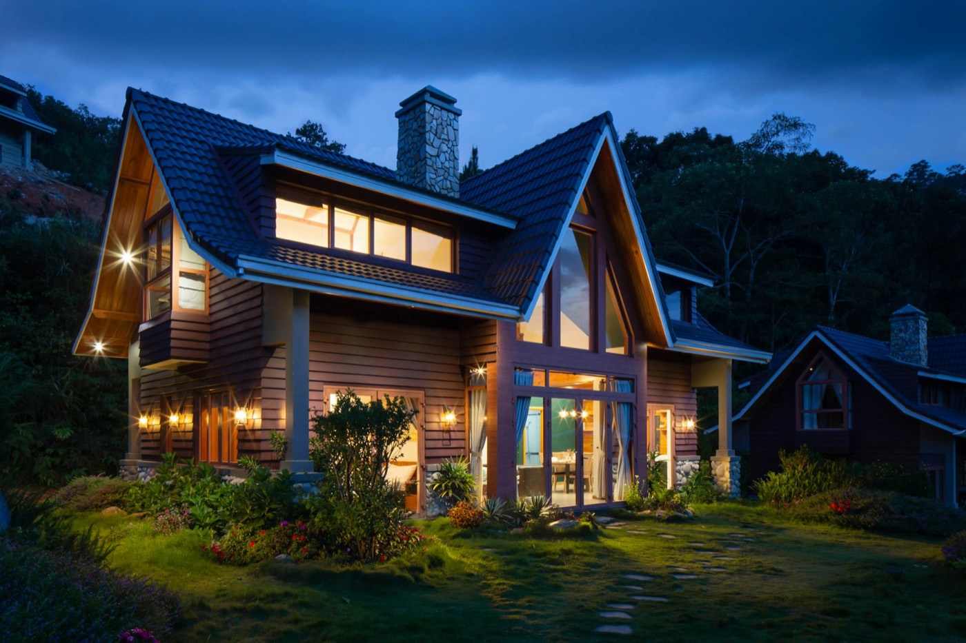 A timber and stone house lit from inside at dusk