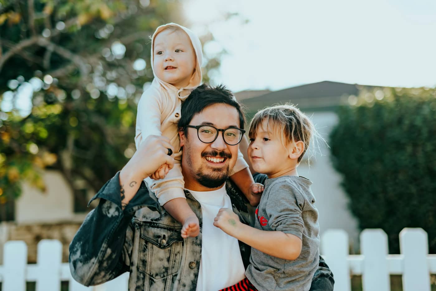 A parent holding their two young children outside a home